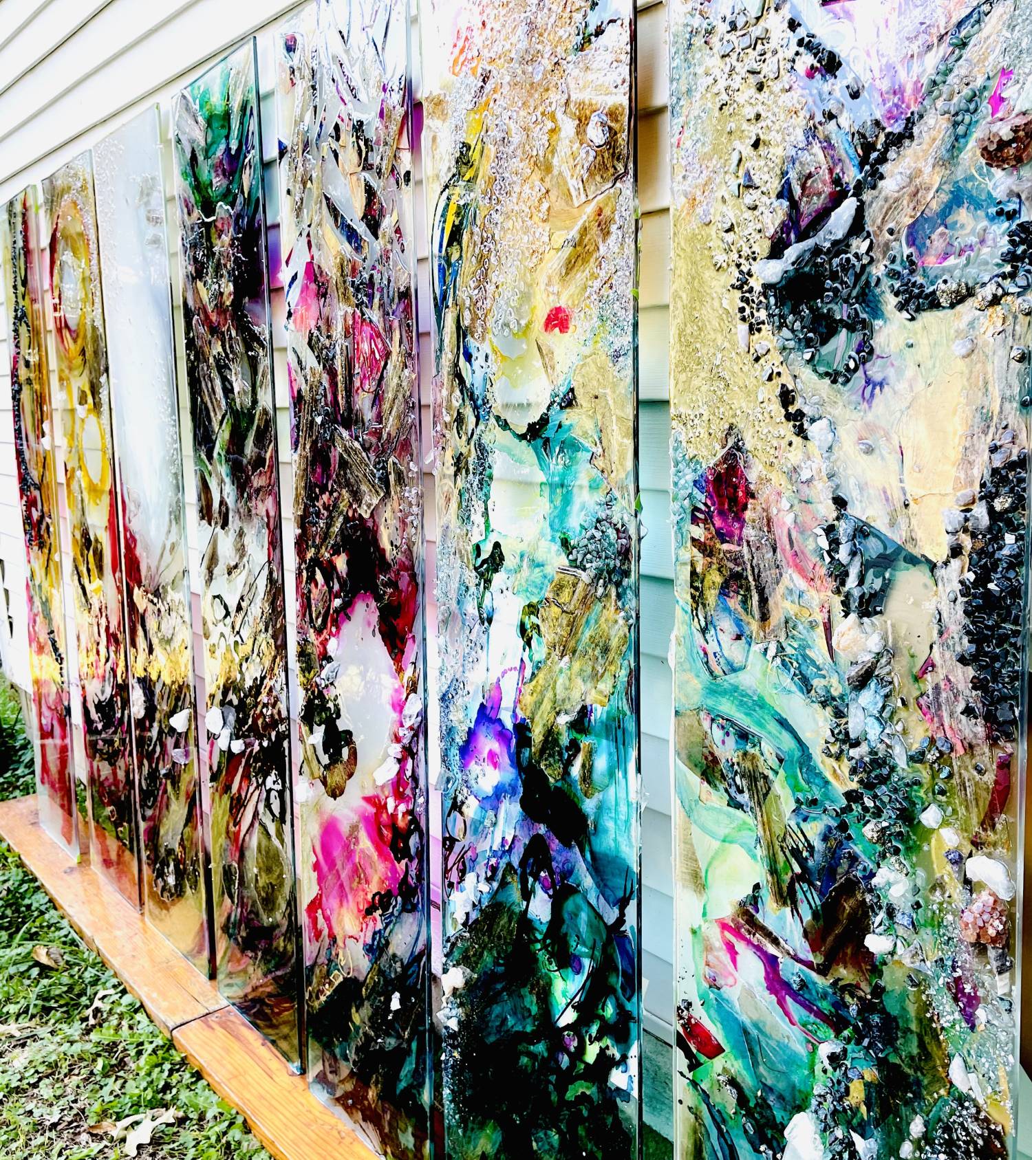 Angle photo of Tammy Campbell's artwork across 7 panels. Mixed media including gemstones in abstract shapes with continuity from one panel to the next. Prominent colors include teal, pink, gold, white, green.