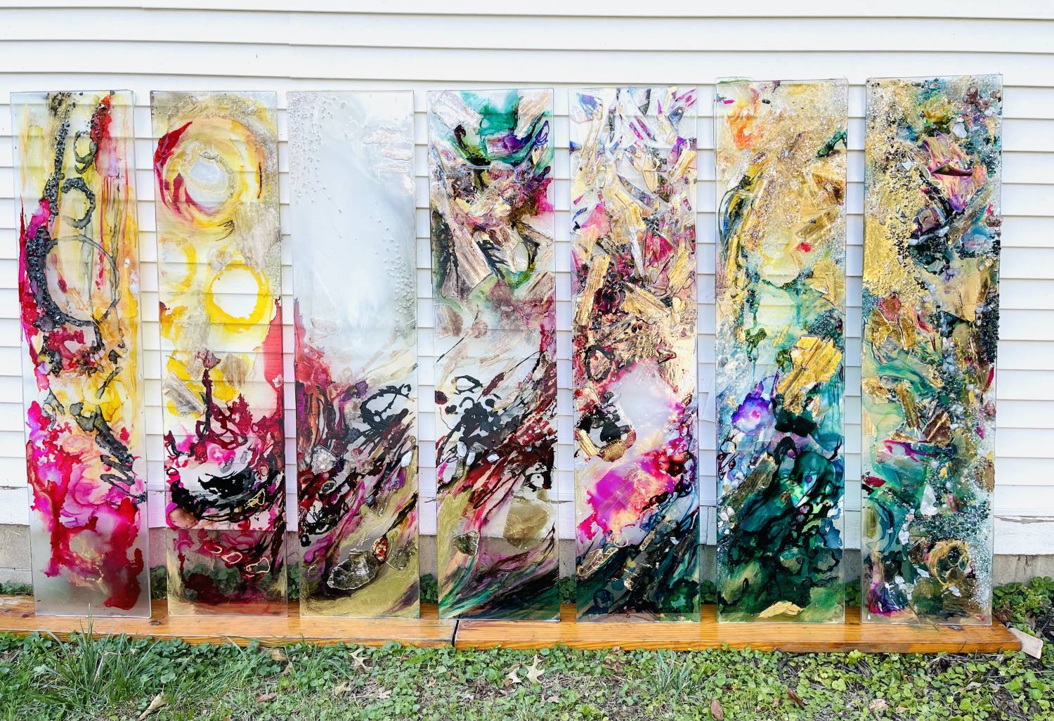 Photo of artwork in 7 tall skinny clear panels. Abstract & multicolored, the artwork is continuous from one panel to the next.