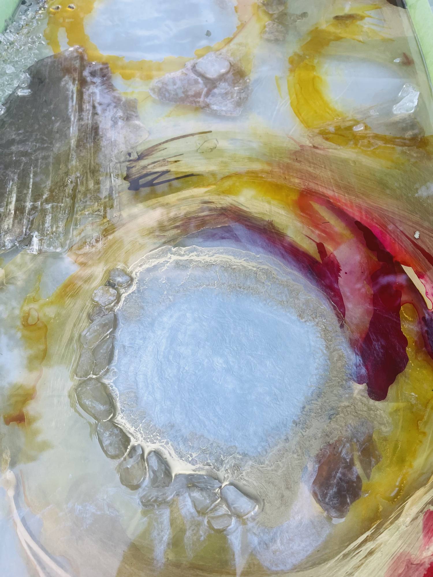 Close up of Tammy Campbell's abstract artwork featuring a circlular shape in yellow and red with clear gems outlining one side of the circle.